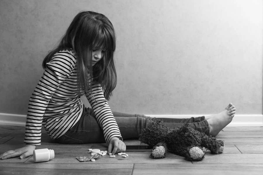 Understanding the Shadow of Alcoholic Parenting - little sitting infront a pile of pills